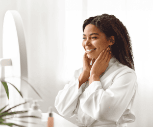 MUlher radiante sorrindo no espelho, usou BB cream e base leve.